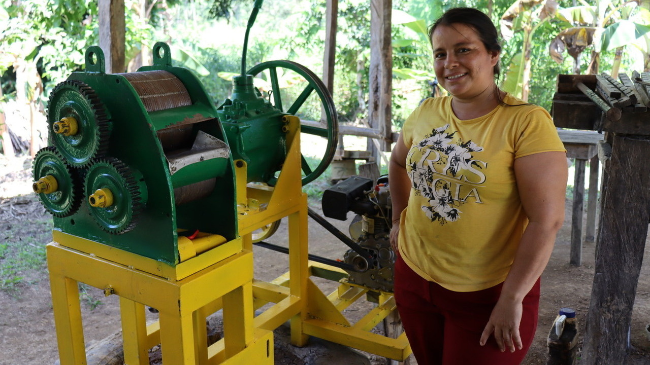 A woman poses next to a sugarcane mill.