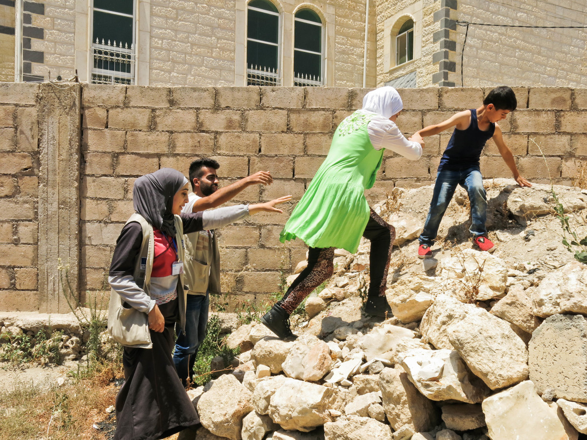 Salalm climbs over a pile of rubble with help from her little brother.