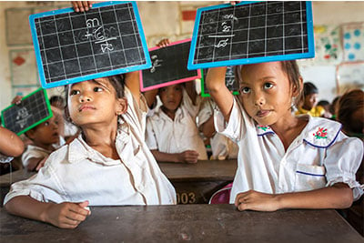 Channa, 7 years old, holds up a blackboard during a mathematics lesson in Cambodia alongside her classmate.