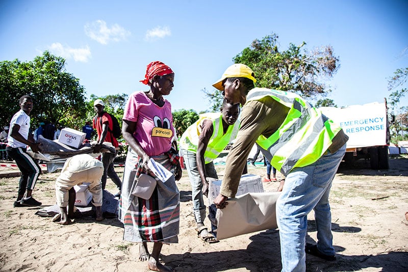 HI volunteers help a woman to collect her items at an NFI distribution point in Mozambique