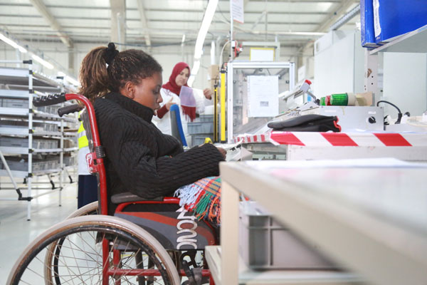 A young woman in a wheelchair working in a factory making eletrical goods.