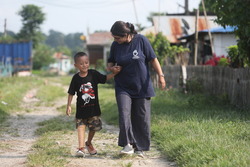 Prabin is walking on a road with Ambika, Prosthetist and Orthotist. © A.Thapa / HI