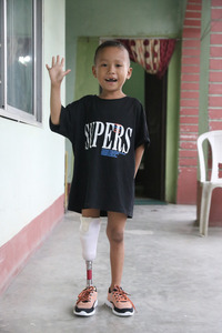 Prabin, standing tall on his new prosthesis, waiving and smiling to the photographer. © A.Thapa / HI