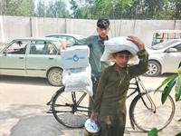 A boy holds an HI food kit on the back of a bike. A younger boy carries food provisions in his hand and on his head.