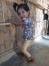 A little girl supports herself on a bamboo bar because she can't stand on her own.