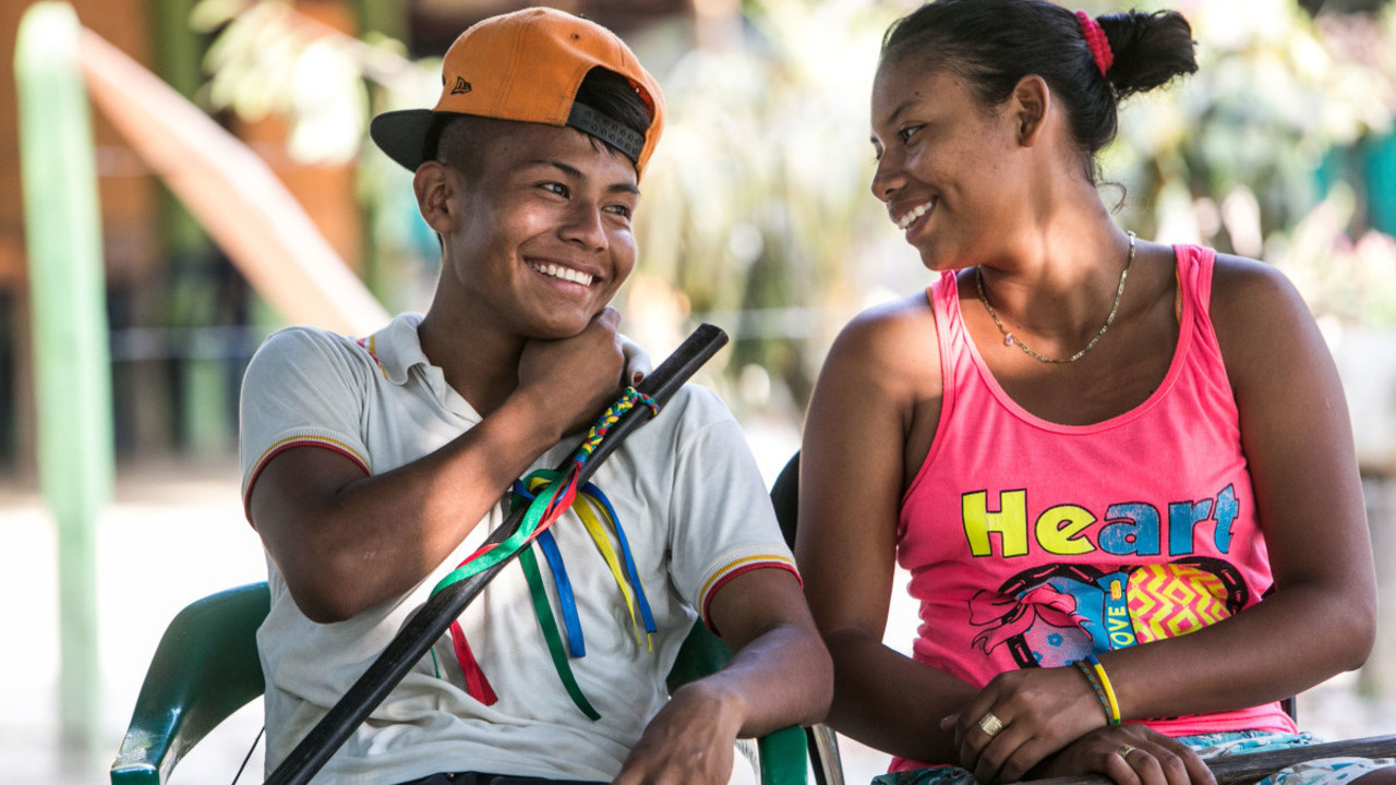 A man and a woman are sitting on chairs, looking at each other and laughing.