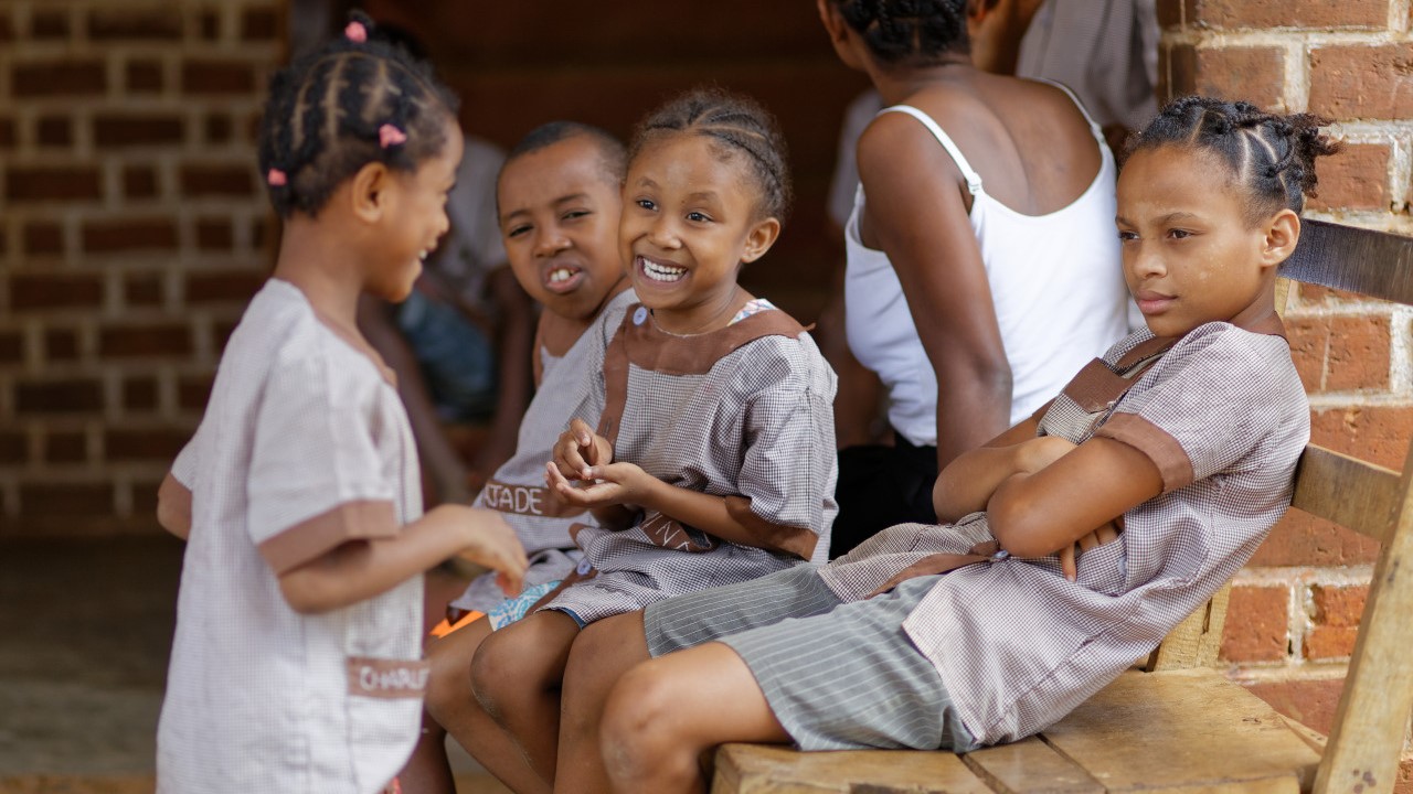Several little girls are gathered in their school playground, laughing together.