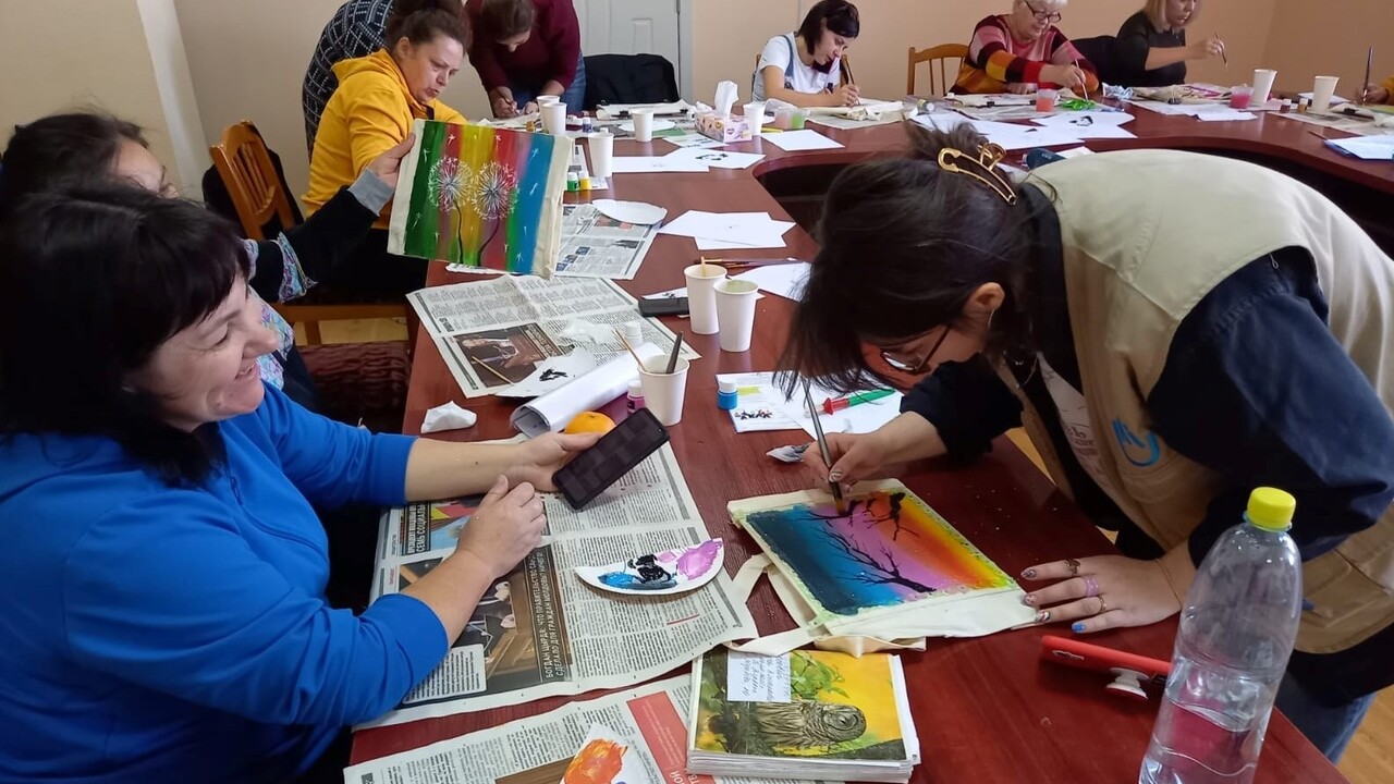  On the right, Carolina from HI and on the left, a beneficiary painting pictures during a psychosocial support group meeting (MHPSS). 