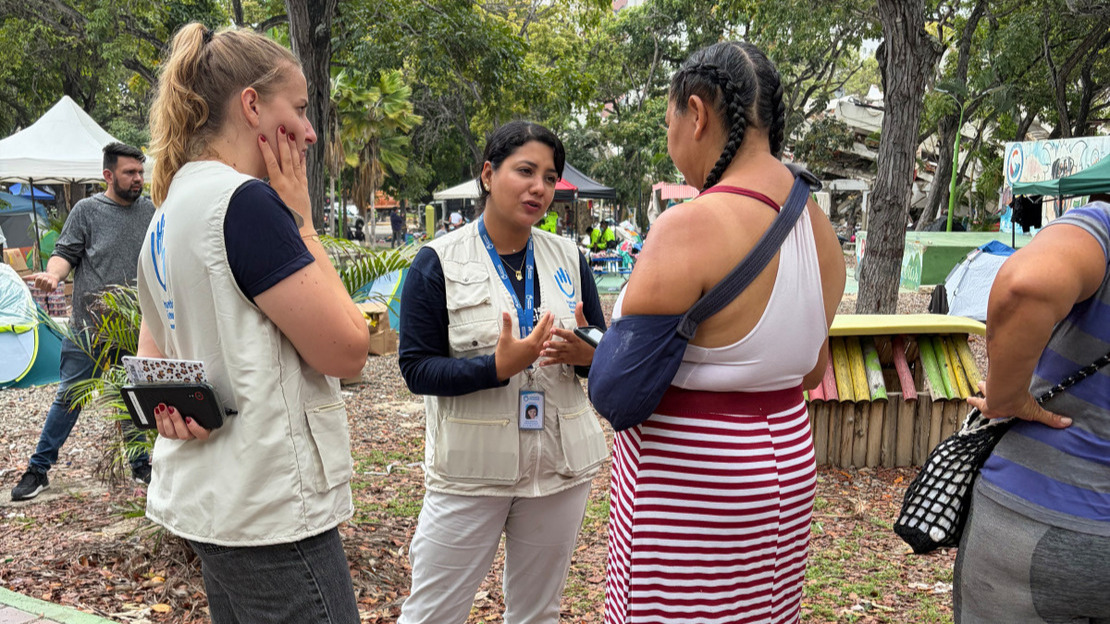 Two women wearing HI jackets are chatting to a third woman who has her arm slung across her shoulder.