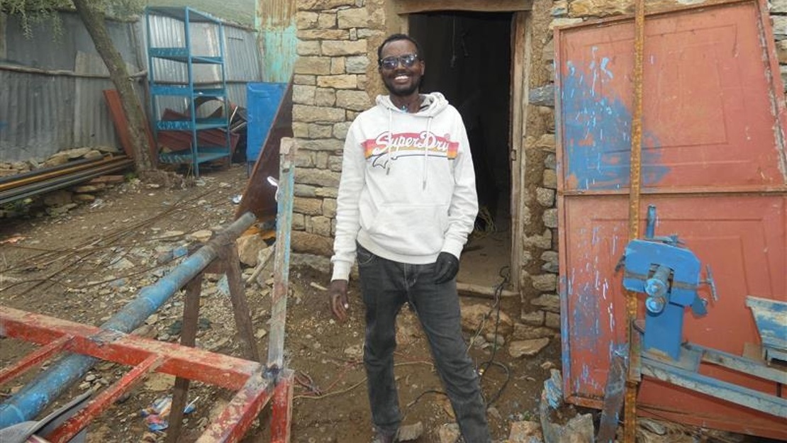 A young men stand in front of is workshop.