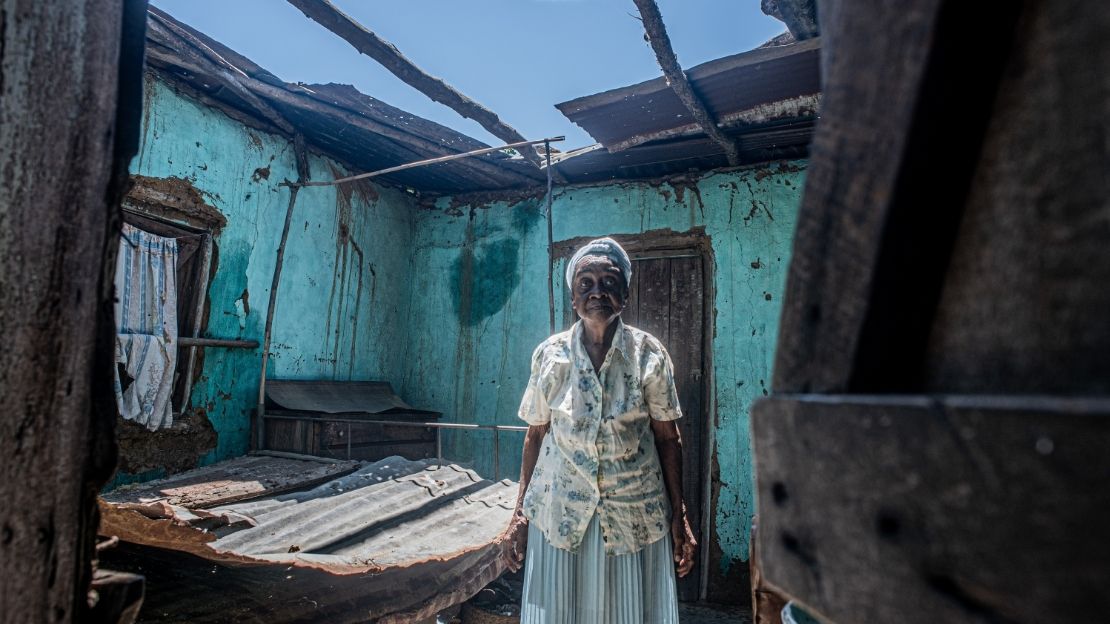 A woman is standing in the middle of a ruined house with no roof.