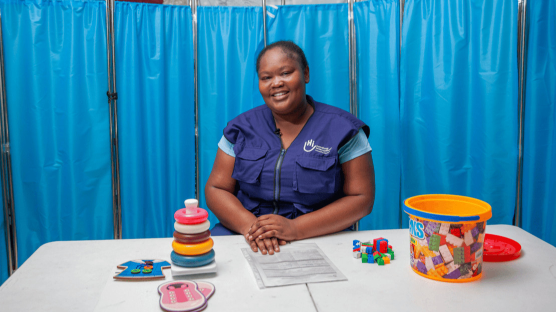 Portrait of a smiling woman sitting at a desk covered with toys and rehabilitation equipment.