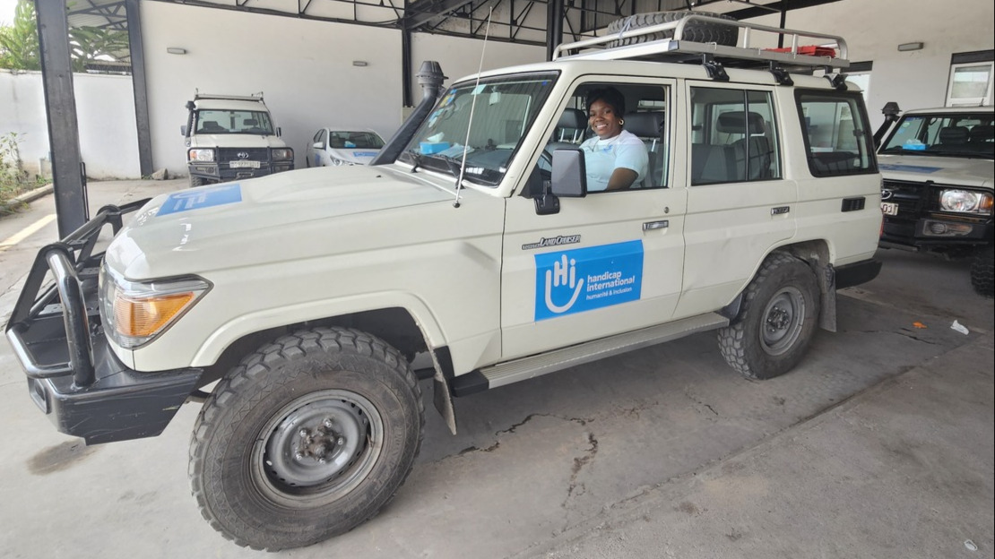 A wide-angle shot of a vehicle parked under a shed, with a smiling woman sitting at the wheel.