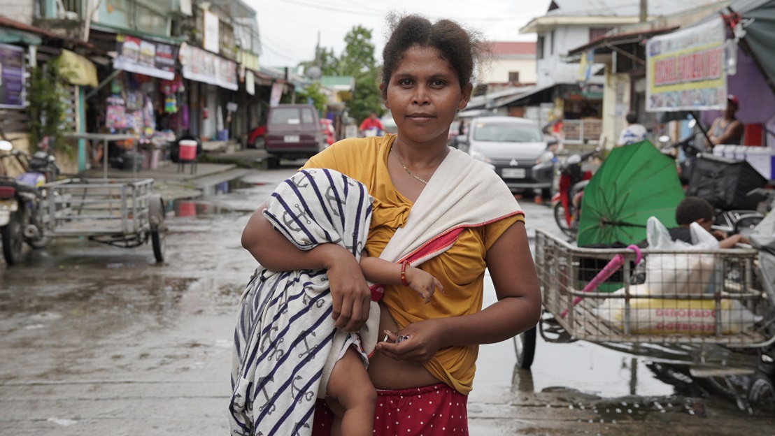 A young woman carries her baby down a street in the Philippines.