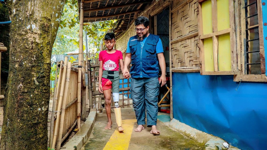 A young boy fitted with a prosthetic leg learns to walk again, holding the hand of an HI care worker.