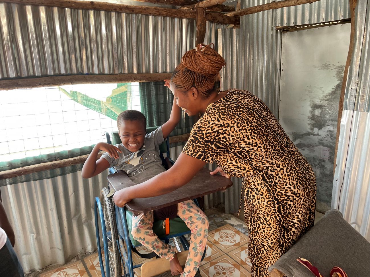 Armele helps her sister, Lydia, into the specially-adapted wheelchair provided for her by HI. 