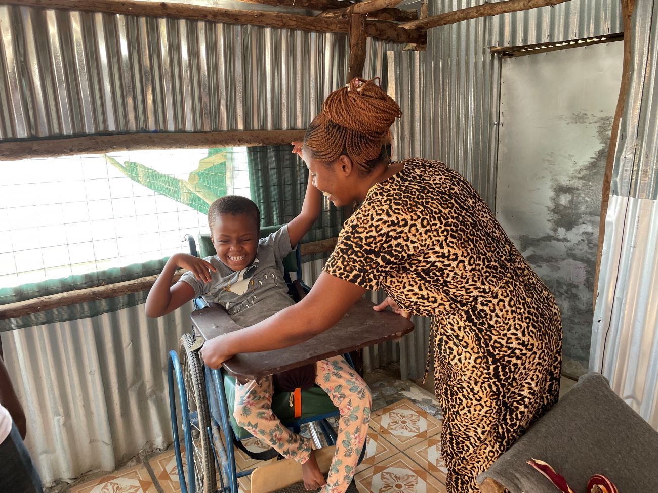 Armele helps her sister, Lydia, into the specially-adapted wheelchair provided for her by HI.