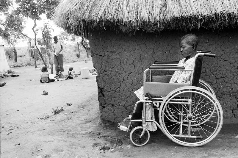 Catarina sitting outside a hut in her wheelchair.