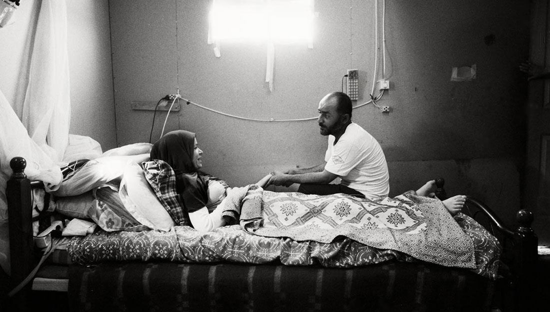 Khouloud in bed with her husband Jamal sitting close by.