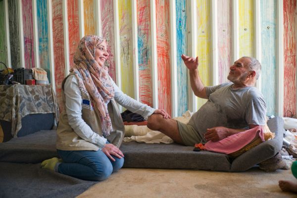 An older man with a lower limb amputation smiles and talks with an HI physiotherapist, Jordan