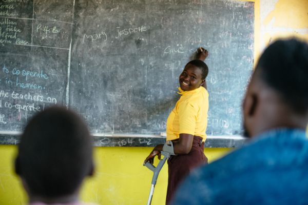 A young girl with glasses holding up an artwork in class.