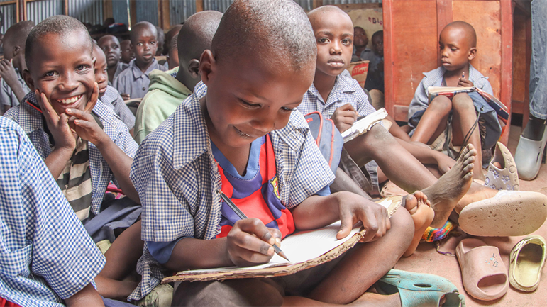 Sidow Mikail Ibrahim is sitting with other children in class and writing on a sheet of paper.
