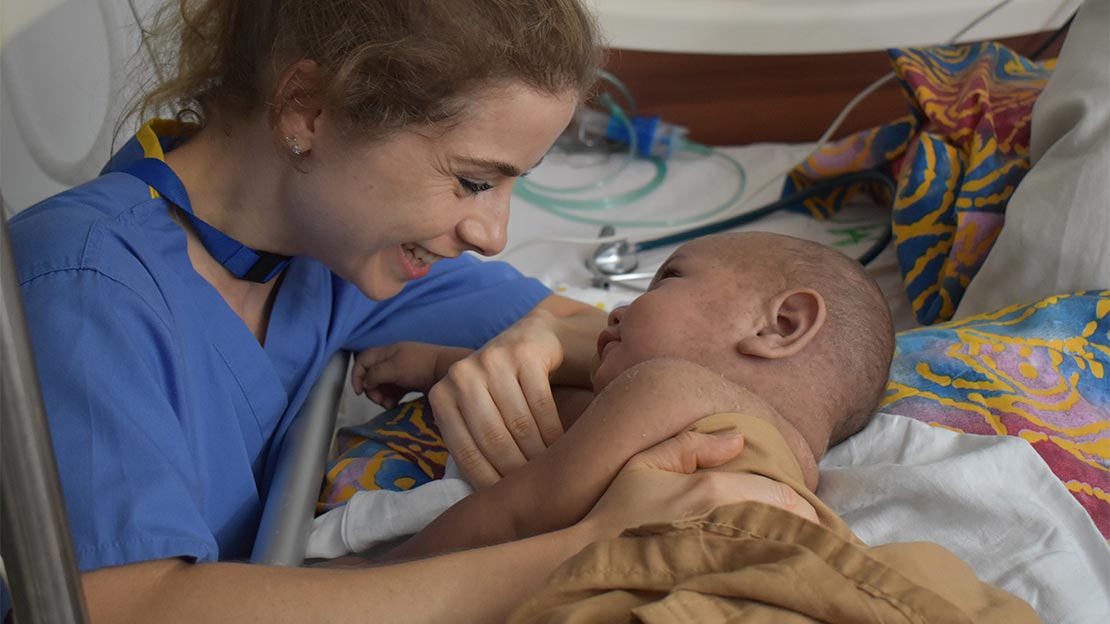 NHS physiotherapist Maeve Tohill reasures a child lying in a hospital bed during the Measles outbreak in Samoa, 2019.