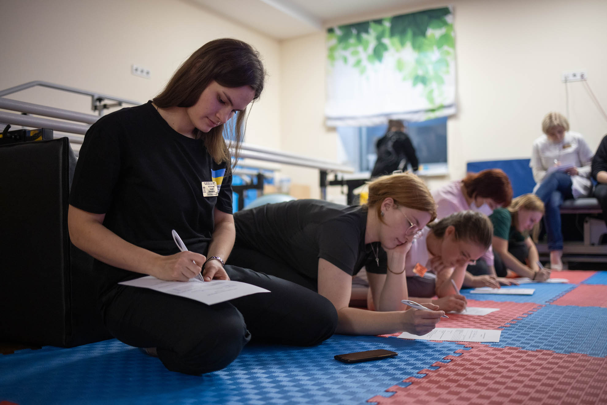 A group of women are sitting on the floor writing on paper.