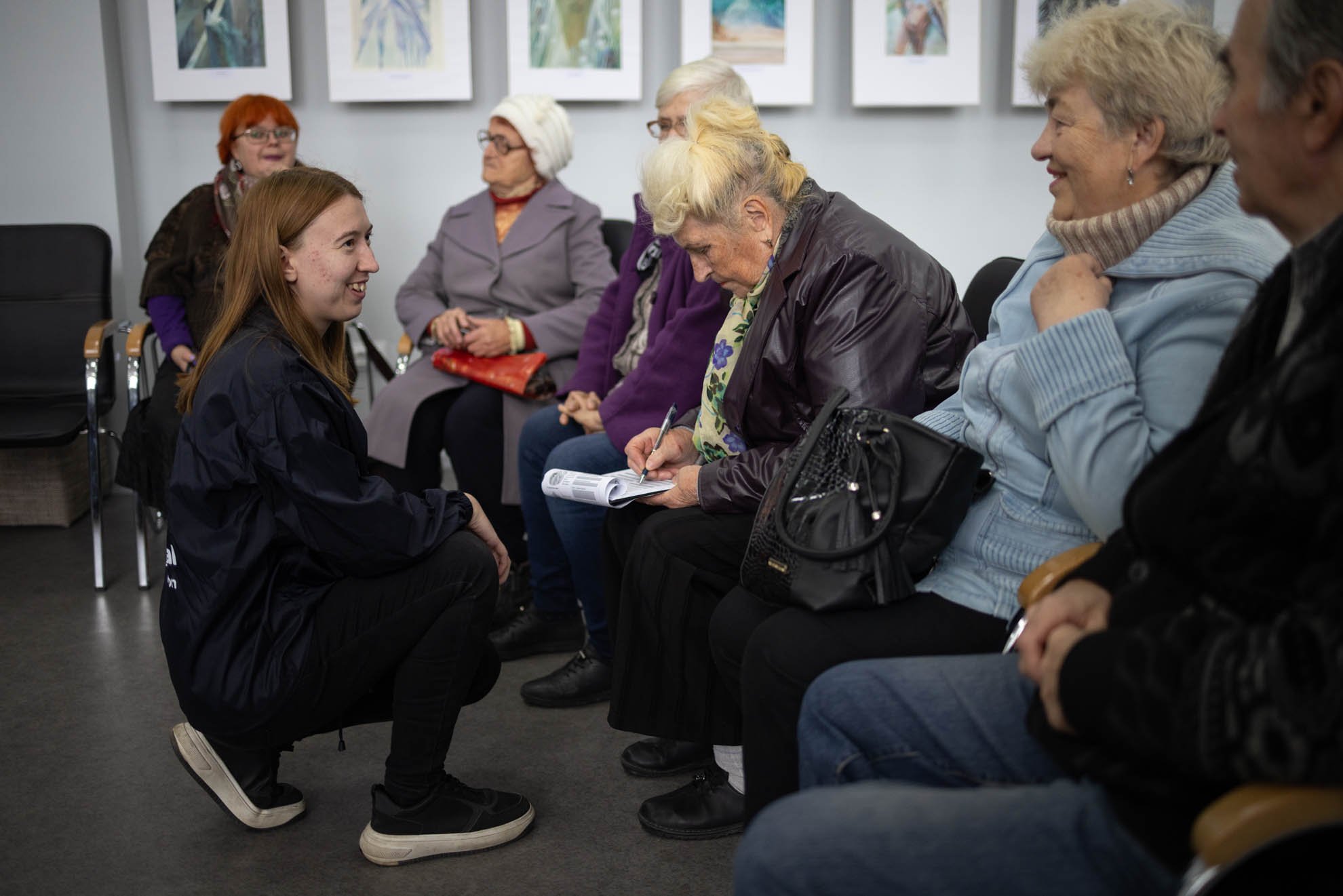 An female HI staff is crouching down and smiling at Olena and other women sitting on chairs in a circle. 