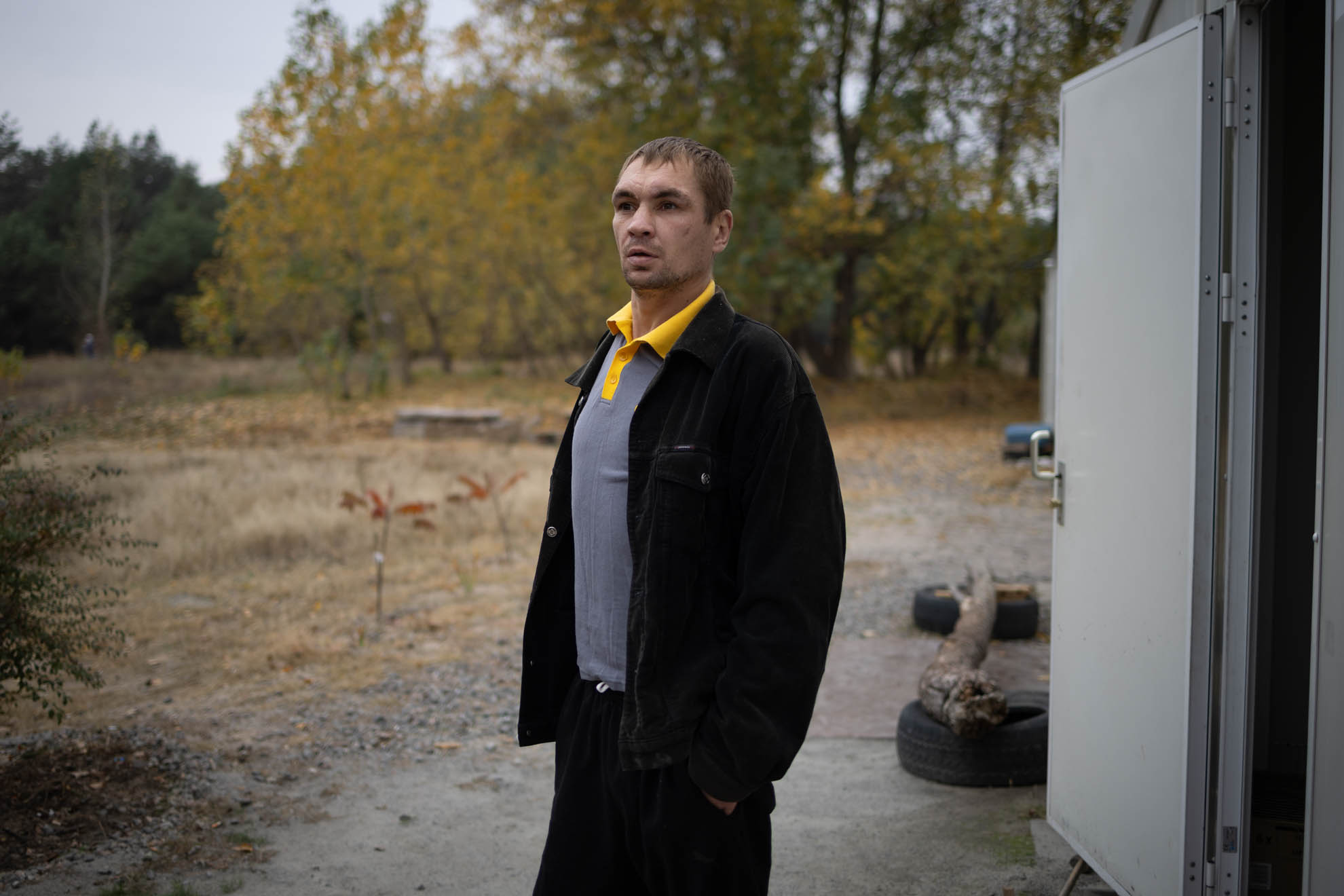 Serhii is standing outside his shelter with his hands in his pockets. 