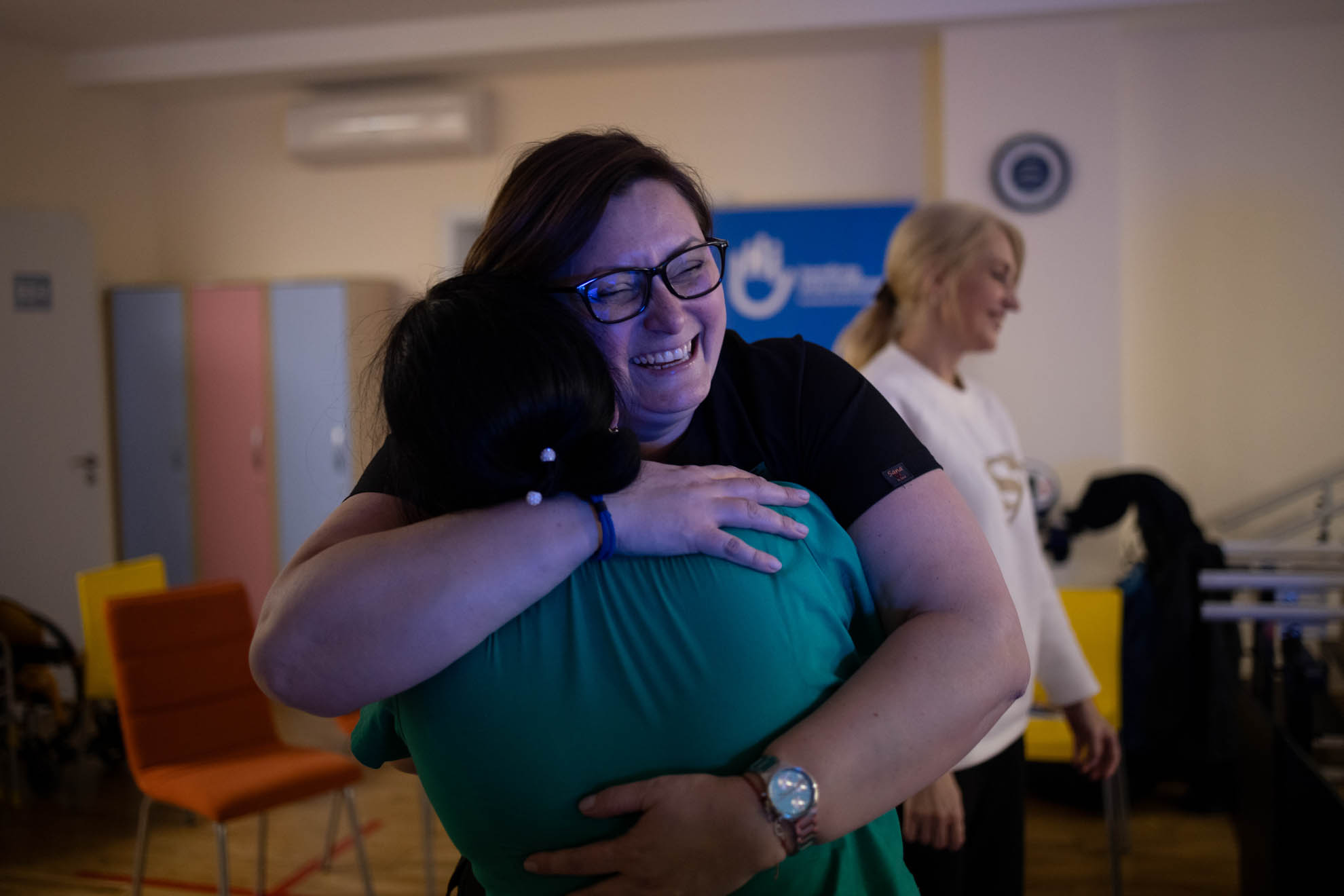 2 persons are hugging. One of them has glasses and is smiling. 