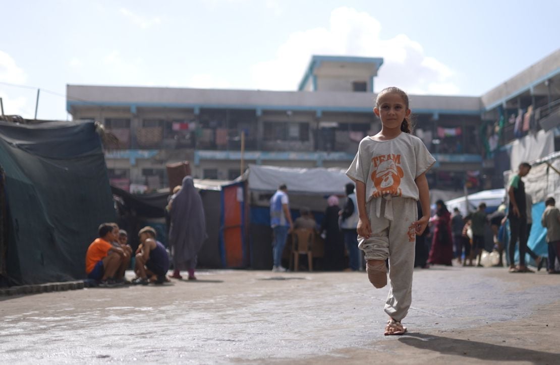 A young girl stands in a large courtyard in Gaza. Her trouser leg is rolled up and it is visible that the lower limb of her right leg has been amputated