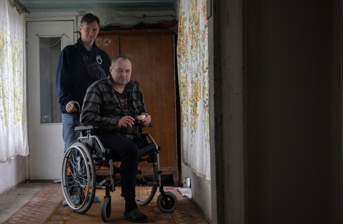 Ukraine Appeal A man sits in a wheelchair with a male HI staff standing behind him