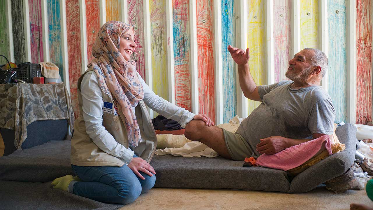 An HI physiotherapist chats with an elderly man with an amputated leg.