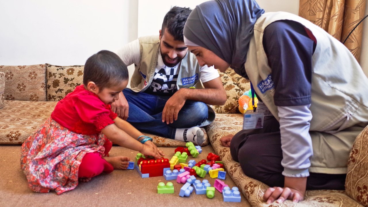 Huda plays with Handicap International staff Abood and Salam as part of a rehabilitation session.; }}