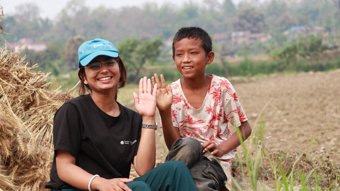 Milan's mother on the left is playing with her son and Bimal, the itinerant teacher. They are sitting on the floor, playing games together.