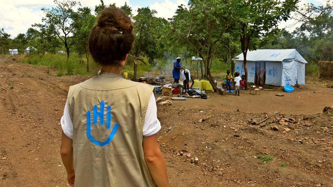 An HI field coordinator with a local family in a refugee settlement in Uganda ; }}