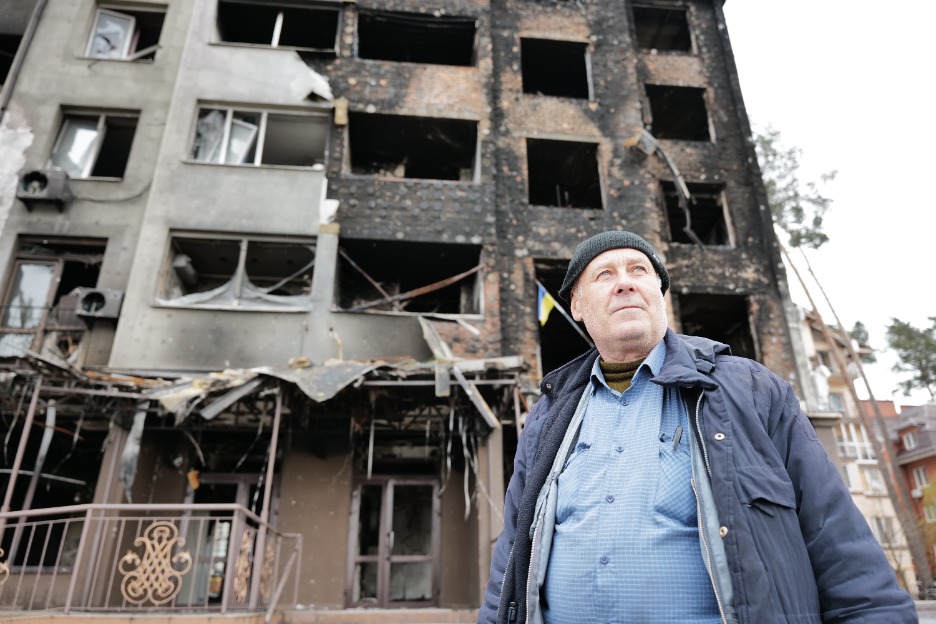 A man stands next to houses destroyed by armed violence in Irpin, Ukraine. ; }}
