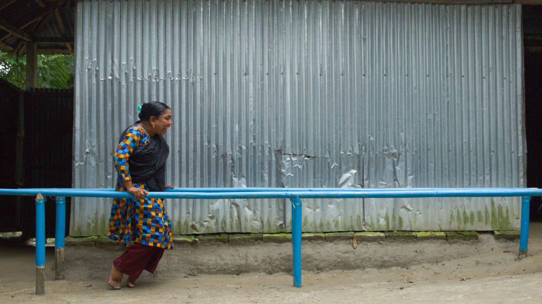 During a rehabilitation session, Anicha manages to walk and do her daily exercises with the help of these parallel bars, supplied by HI.The woman is standing on the frames looking at the camera with a big smile and wear a plaid skirt with different colors bleu orange yellow; }}