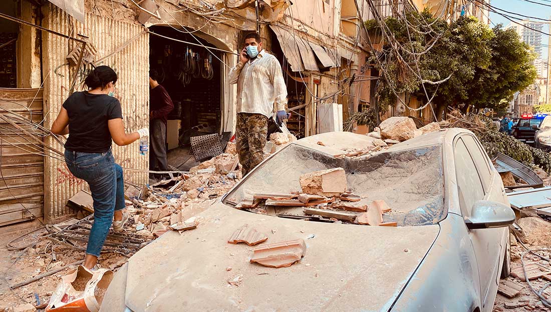 Beirut, Lebanon- August 5: People wearing face masks walks past damaged cars after Tuesday's massive explosion in Beirut, Lebanon. The blast hit Lebanese capital on August 4, with over 80 people killed and some 4,000 injured.; }}