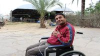 Odai outside in the yard, with the family farm behind him. Gaza.; }}