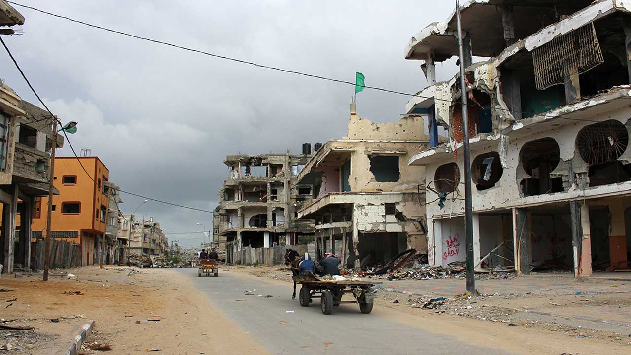 People on horse and cart pass buildings in Shejaiya, Gaza. The area is heavily contaminated with ERW and many people are still living amongst the rubble.; }}
