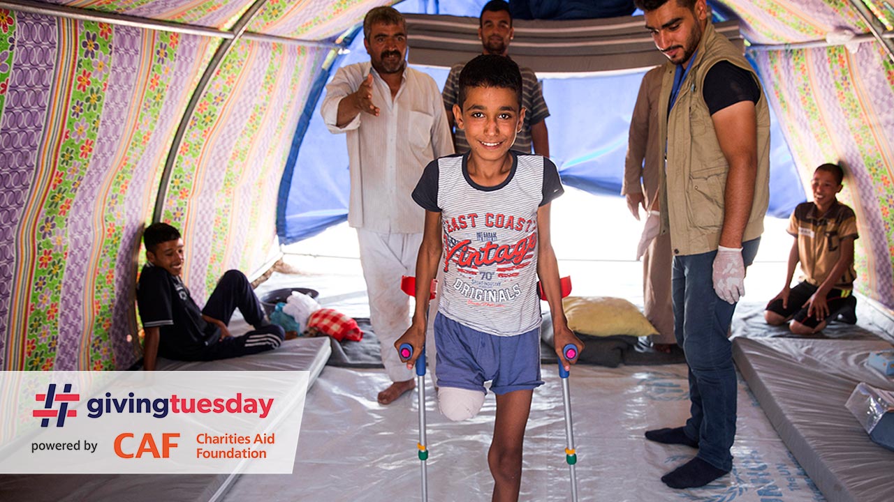  Abdel Rahman stands with crutches in his tent, while HI physiotherapist Mohammed looks on.; }}