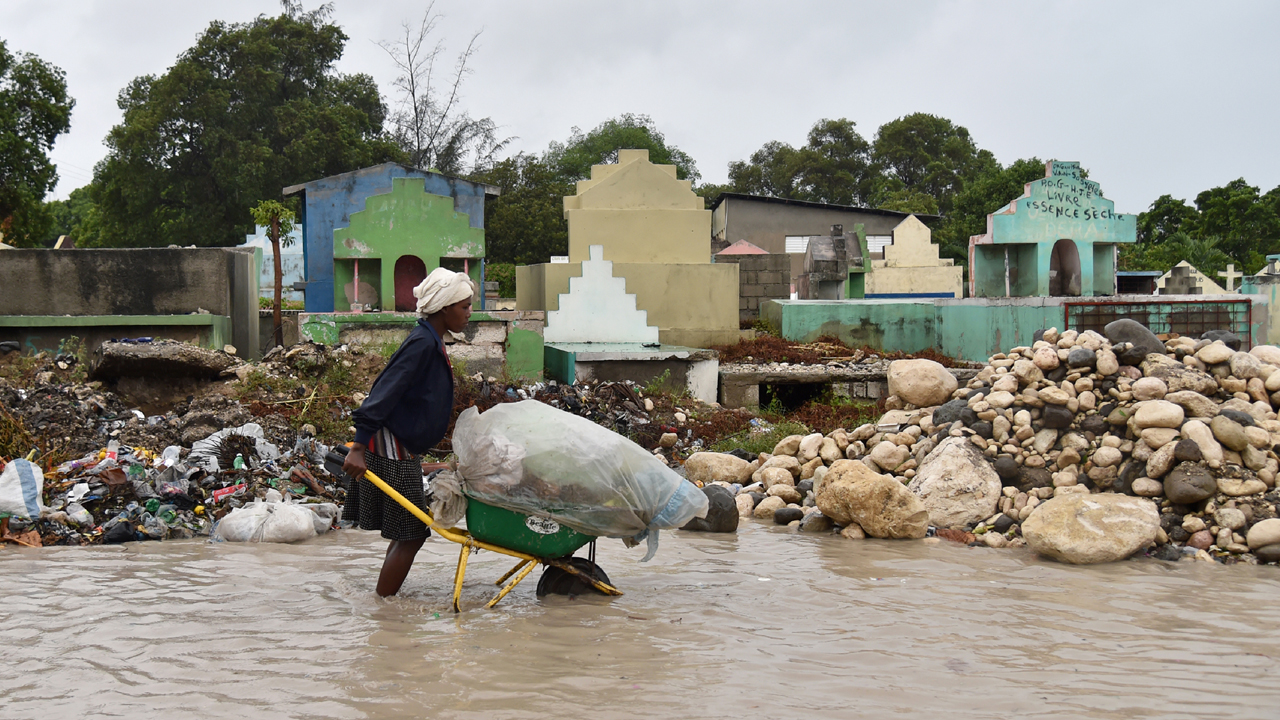 A woman pushes a wheelbarrow while walking in a partially flooded street, in the Haitian capital, Port-au-Prince, on October 4, 2016.; }}
