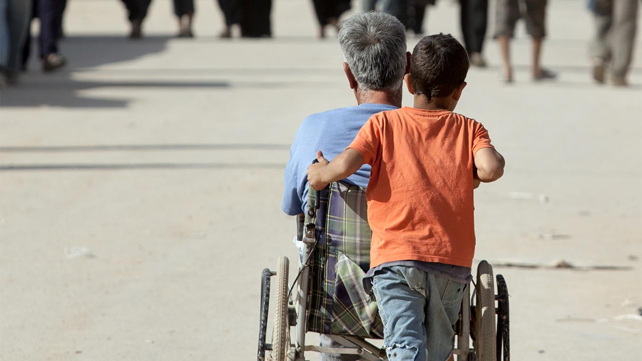 A child pushes a man in a wheelchair in Zaatari refugee camp, northern Jordan.