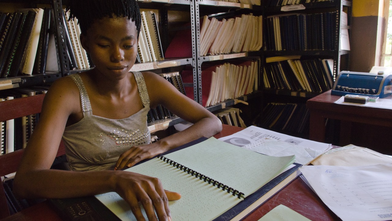 A student at the Milton Maragai School for the Blind in Freetown, Sierra Leone, reads a Braille Ebola Prevention Guide produced by Handicap International.; }}