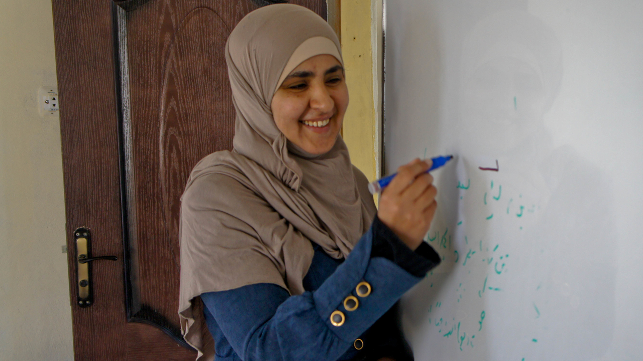  Ashwaq, wirting on a white board in the centre that she founded, Jordan.; }}
