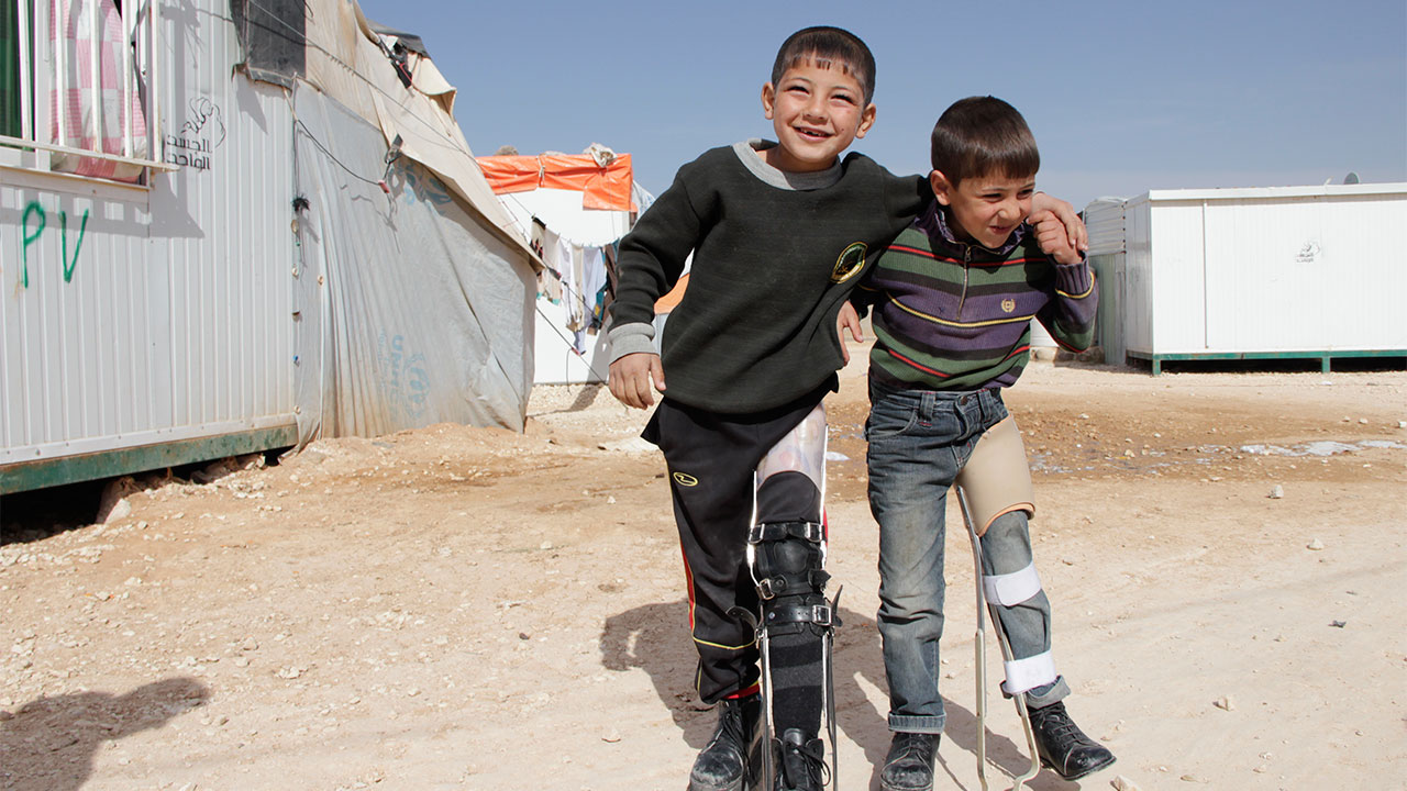 Mahmoud, 7, outside walking, supported by his friend and his orthosis.
